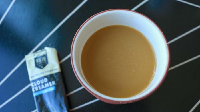 A cup of coffee with an unused Kuju Coffee Cloud Creamer satchet beside it.