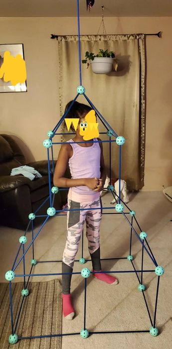 A reviewer's photo of their child standing proudly inside a fort they've built.