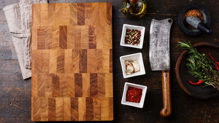 A large end-grain cutting board placed on a table, accompanied by a cleaver and spices.