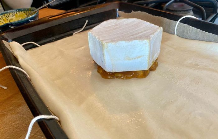 A wheel of brie rests on top of jam in the middle of a puff pastry sheet.