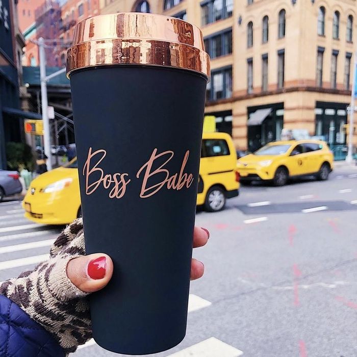a hand holding the Boss Babe rose gold and matte black travel mug on a bustling city street