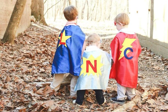 Three young models dressed in vibrant capes featuring their first initials on the back.