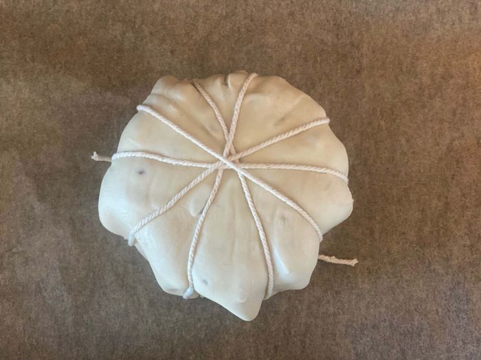 A baked brie ready for baking, with strings tied around it in a star pattern.