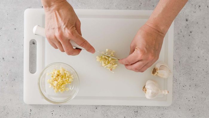 A person chopping garlic on a plastic cutting board.
