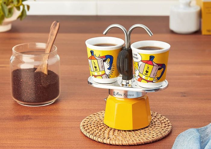 The bright yellow pot alongside two espresso cups.