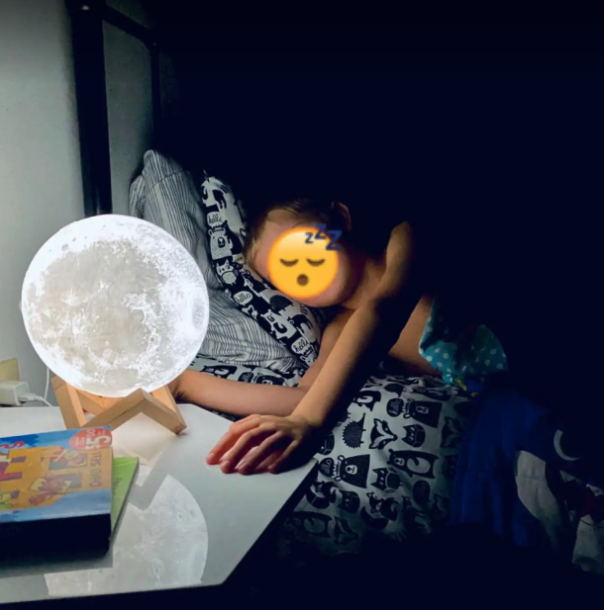 A child's bed, with the moon lamp glowing softly on the side table.