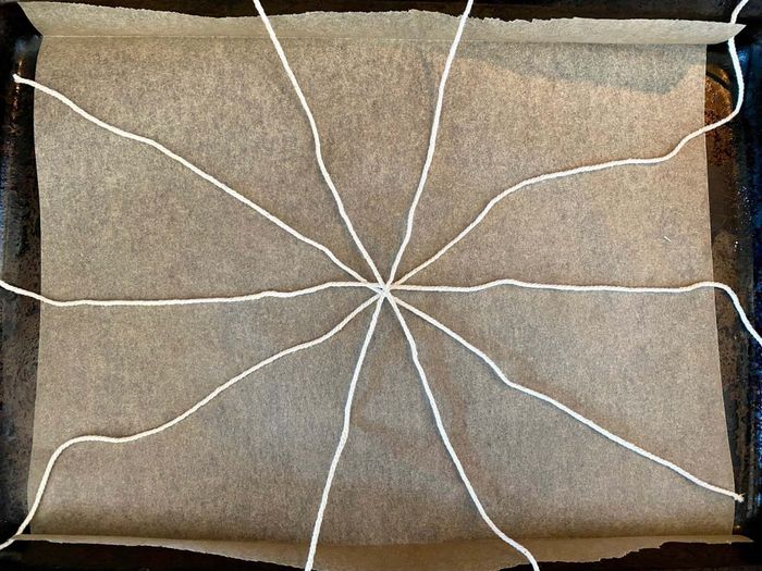 A piece of kitchen twine arranged in a star shape on a baking sheet.