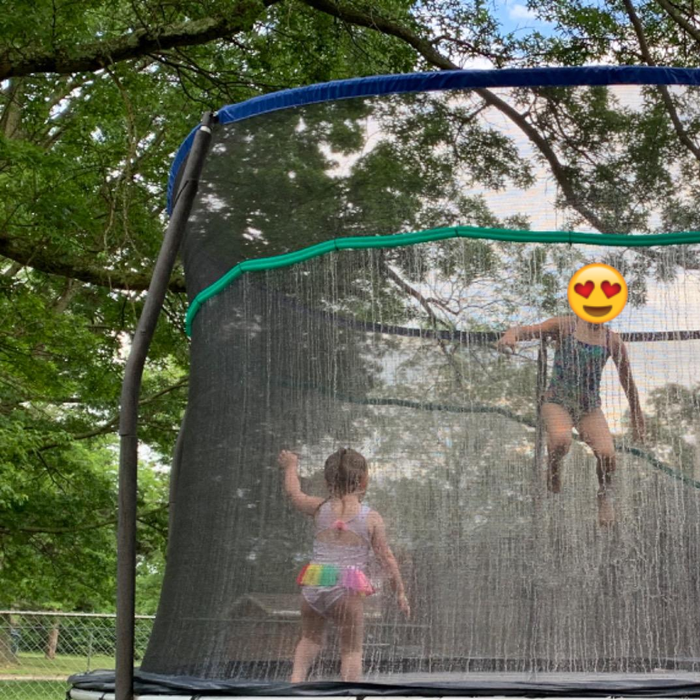 Children enthusiastically jumping on the trampoline while the sprinkler hose sprays water over them, creating a fun, wet adventure.