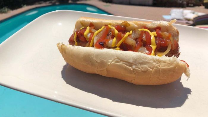 A plate with a hot dog topped with ketchup, mustard, and onions.