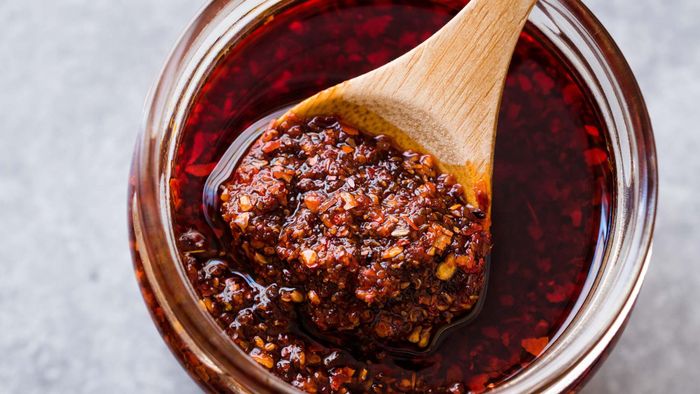 A jar of chili crisp with a spoon resting inside.