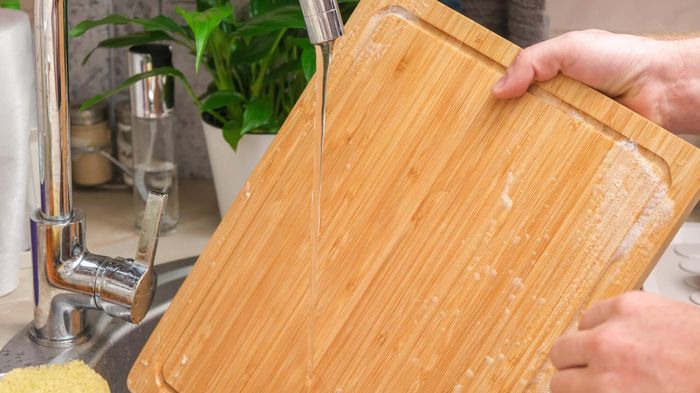 Someone washing a bamboo cutting board in the sink.