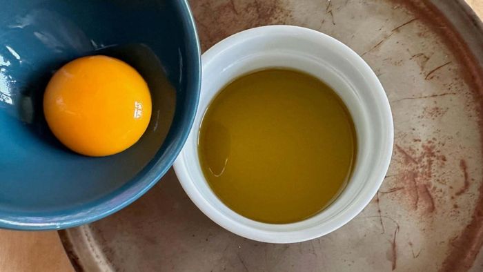 The egg yolk being carefully lowered into the ramekin filled with warm oil.