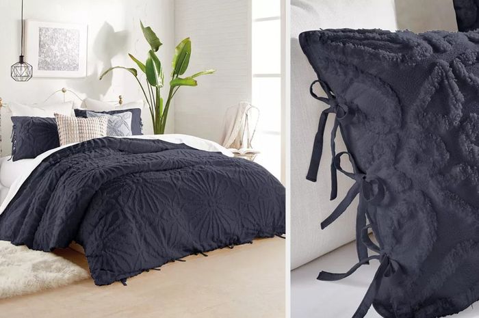 A black medallion tufted comforter paired with matching pillows and throw pillows, set against a white wall next to a large house plant, creating a cozy yet stylish atmosphere.