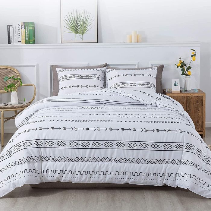 A black and white arrow and boho striped print comforter with matching pillows placed next to a wooden side table adorned with plants on top, blending style with nature.