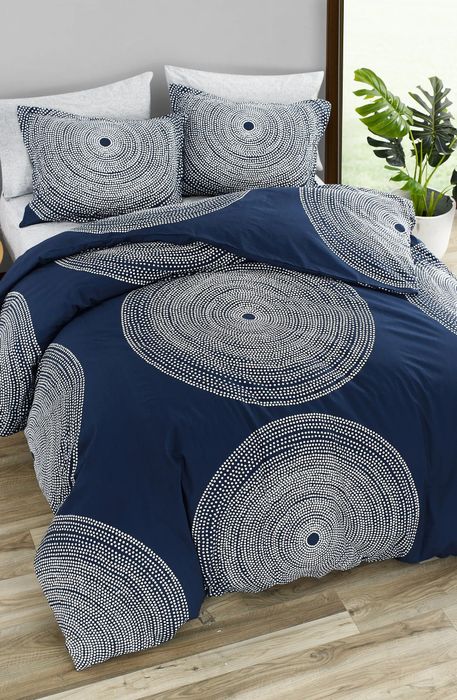 A navy blue comforter featuring large white spotted circles, paired with matching pillows, set against a sleek gray wall for a modern and bold look.