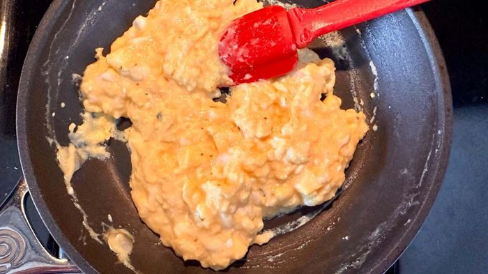 Scrambled eggs cooking in a pan with a red spatula.
