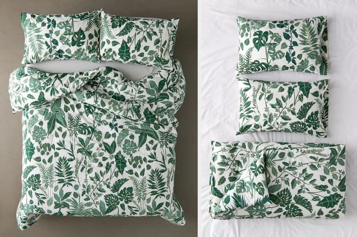 A white and green leaf printed comforter, with matching pillows on crisp white sheets, showcasing a close-up view of the pillows and comforter neatly folded on top of the sheets.