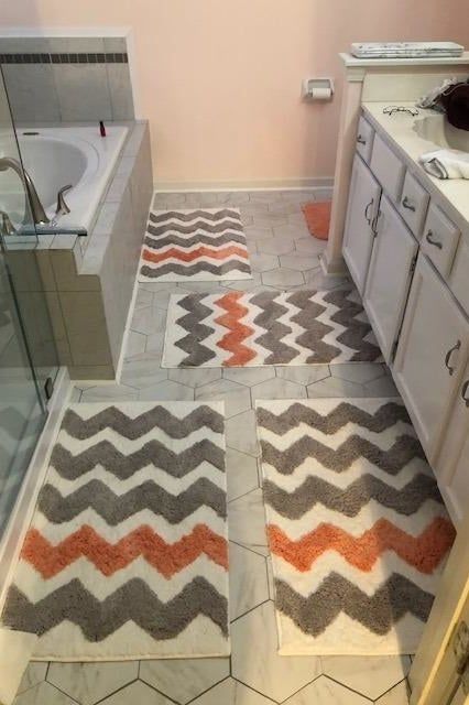 A reviewer’s photo showing four gray and orange striped bath mats arranged in a bathroom.