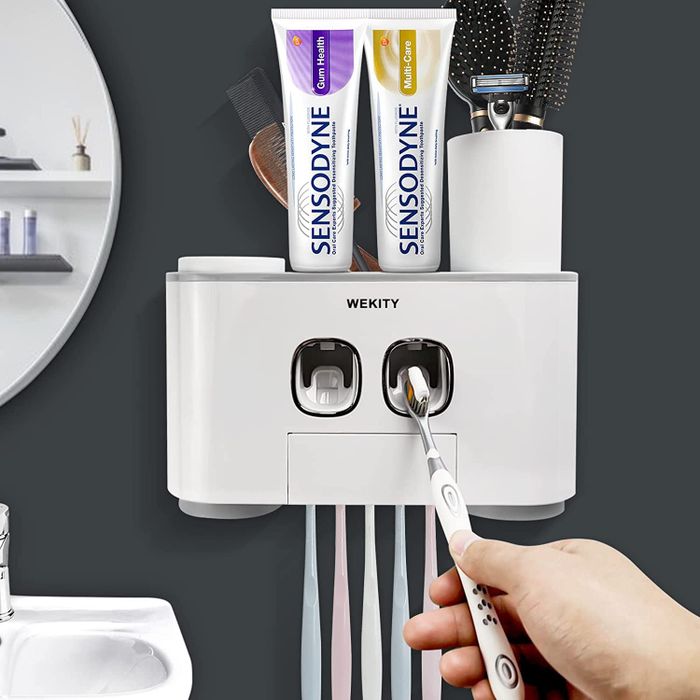A person demonstrating the automatic toothpaste dispenser by holding a toothbrush up to it.