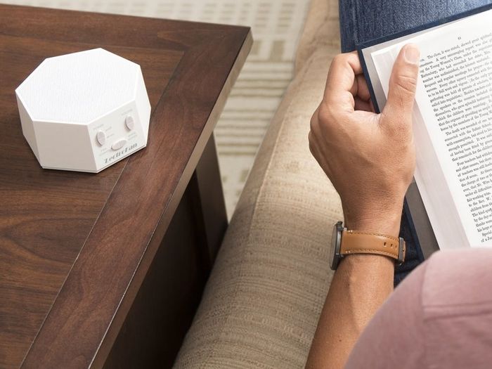The white noise machine placed on a side table while a model reads a book