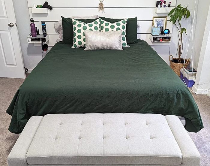 Image of a dark green duvet cover with matching pillows and polka dot throw pillows, placed behind a tufted ottoman.