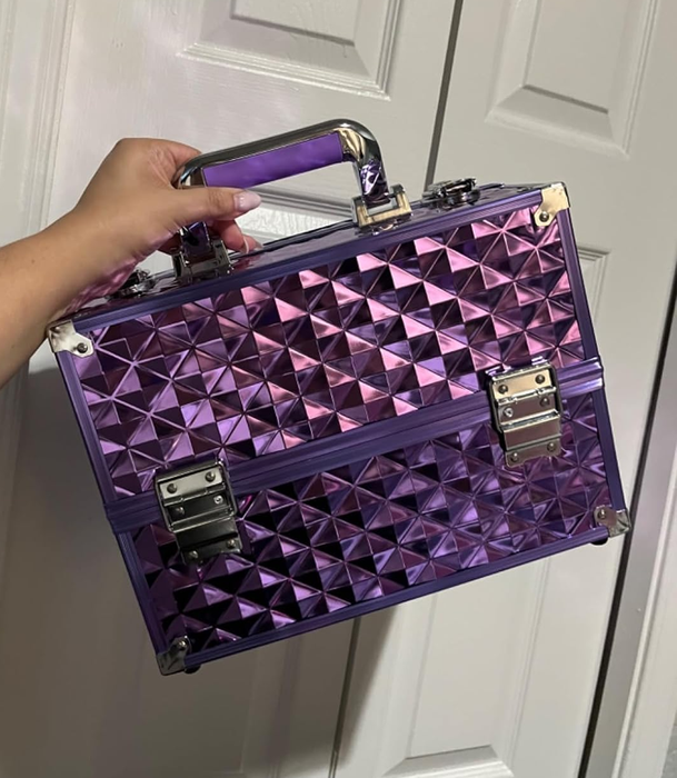 A person holding a sleek, metallic makeup case with a geometric pattern and handle, ideal for organizing cosmetics.