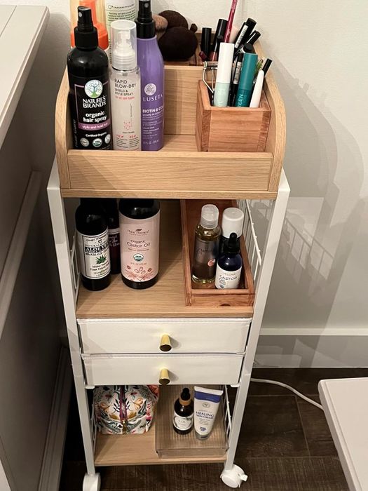 A bathroom organizer featuring a variety of skincare and personal care items, from lotions to oils and sprays, all neatly arranged on a stylish wooden and metal cart.