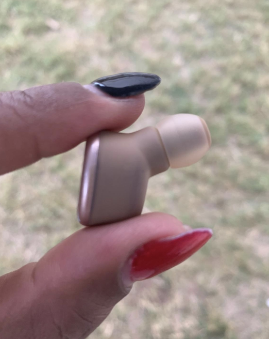 A reviewer holding up an earbud to demonstrate its compact size
