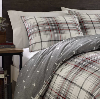 A close-up shot of a comforter with a gray side and a white deer pattern, next to a brown side table