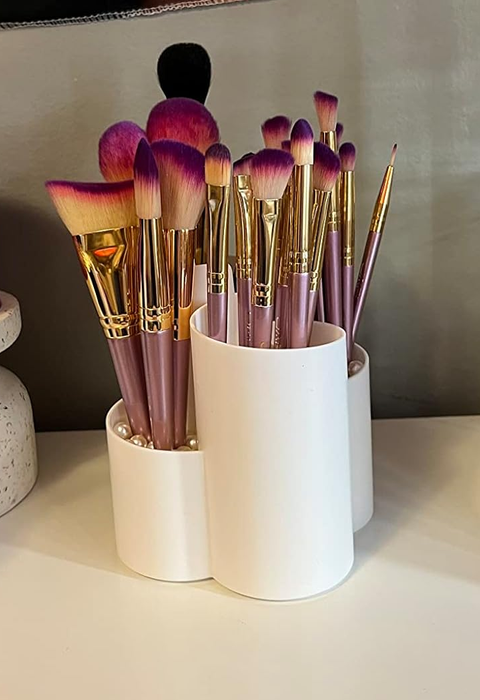 A collection of makeup brushes with pink and purple tips arranged in a white holder on a countertop.