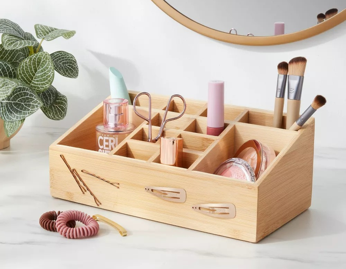 A wooden makeup organizer resting on a marble countertop, surrounded by a variety of beauty essentials such as brushes, scissors, and creams.