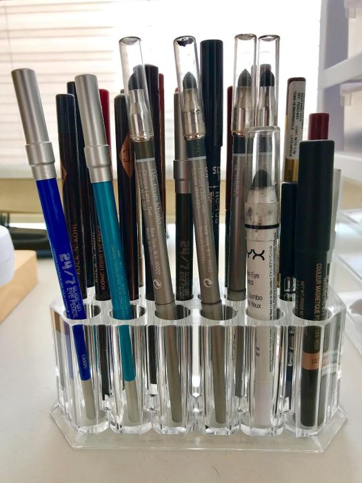 A variety of eyeliners and cosmetic pencils are neatly arranged in a clear holder, displayed on a white surface for easy access.