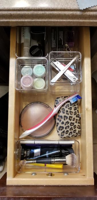 A perfectly organized drawer featuring clear containers filled with makeup and toiletries