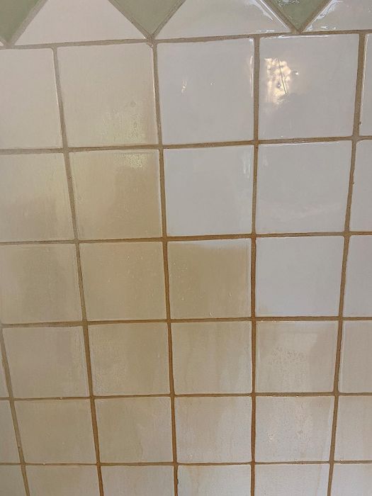 A before-and-after image of a bathroom tile, partially cleaned with The Pink Stuff.