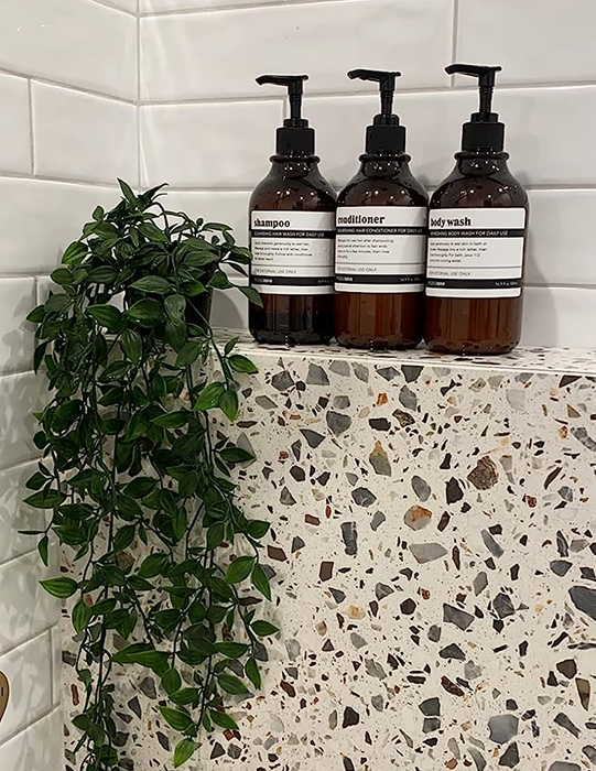 A reviewer’s image showing their shampoo, conditioner, and body wash bottles neatly placed on the wall of a shower.