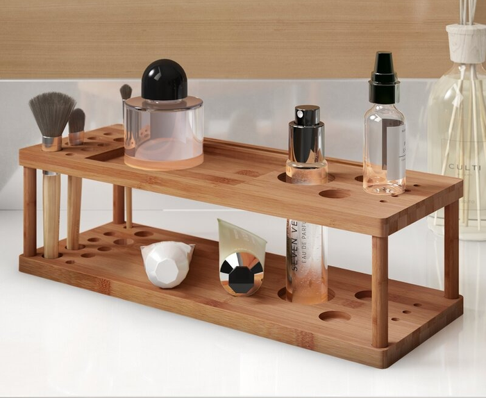 A bamboo makeup organizer displayed on a bathroom counter, containing brushes, foundation, serums, and other beauty products.