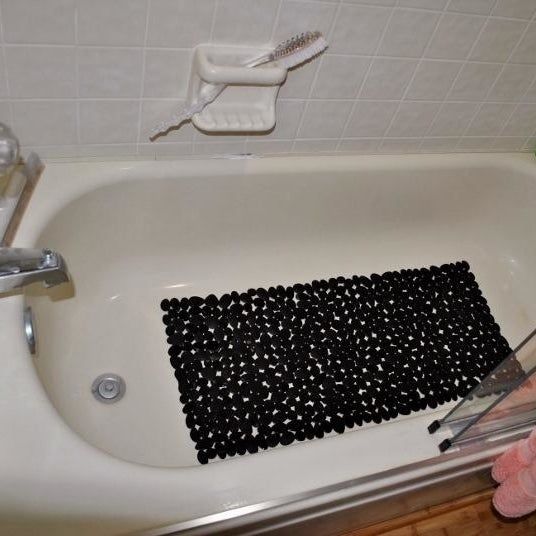 A reviewer’s photo showcasing the black pebble bath mat inside a bathtub.