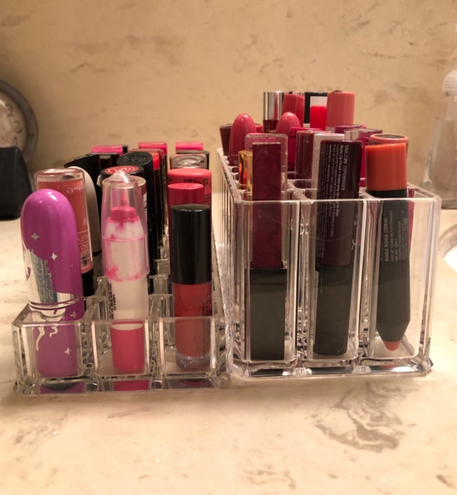 A clear holder on a bathroom counter neatly arranges a variety of lipsticks and lip glosses for easy selection and quick access.