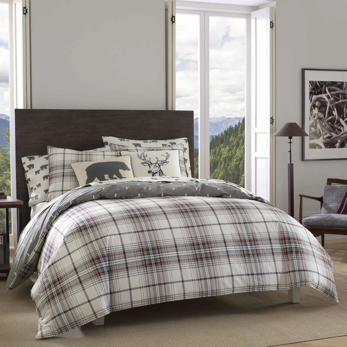 A reviewer image featuring a gray, black, and white plaid comforter and matching shams, with a bear throw pillow and deer throw pillow placed on a brown carpet