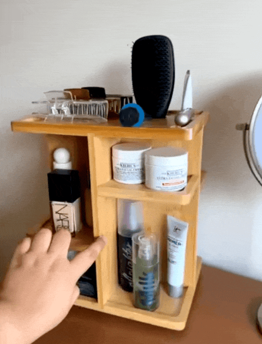 A spinning wooden organizer on a table, storing various skincare products, hair care items, brushes, and other beauty essentials.