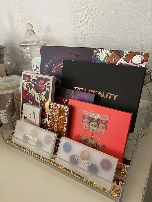 A collection of makeup palettes and beauty items arranged in an organizer, featuring Tati Beauty, alongside decorative cards and packaging