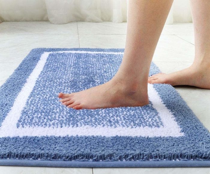 Lifestyle image of a person stepping onto a plush blue bath mat, showcasing its soft texture and elegant design