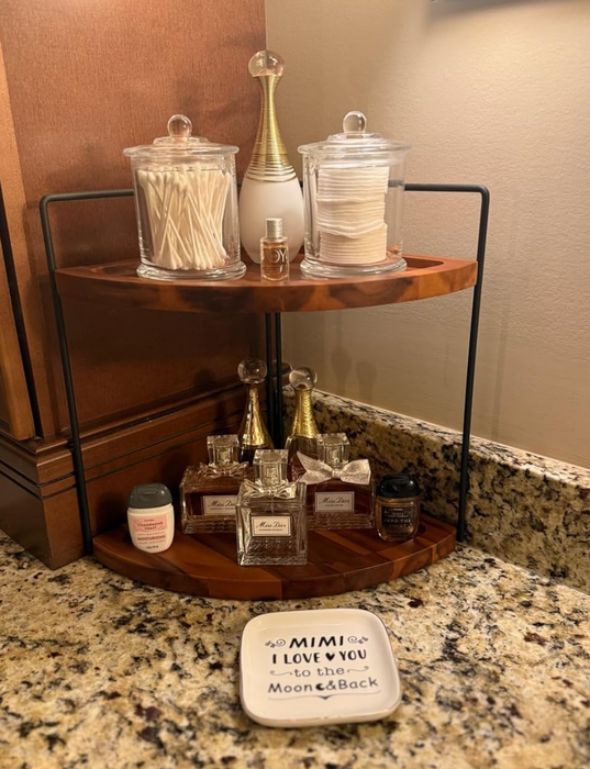 A bathroom counter featuring a two-tier shelf neatly storing cotton swabs, pads, perfumes, and lotions