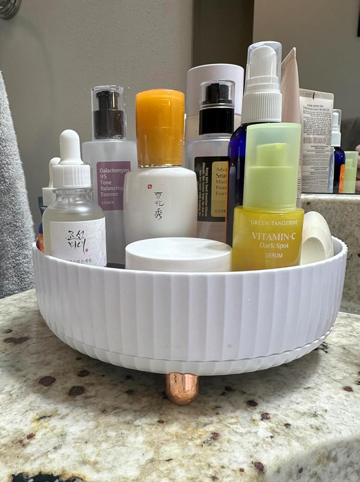 An assortment of skincare products, including serums and lotions, neatly placed in a white organizer on a bathroom counter.