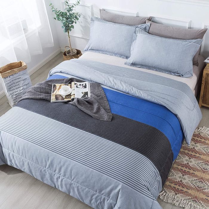 A white, gray, and cobalt blue striped comforter set with matching shams, with an open book resting on top next to a houseplant, combining relaxation and style.