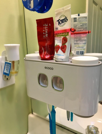 The white stand is mounted on a mirror and has spaces for two toothpaste tubes and two toothbrushes.