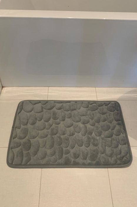 A reviewer image showing a gray cobblestone-patterned memory foam bath mat placed next to a toilet and bathtub.