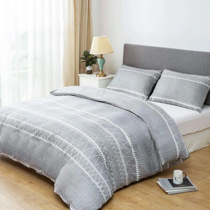 A gray and white striped boho duvet cover paired with matching pillowcases resting on white sheets, all set against a clean white wall.