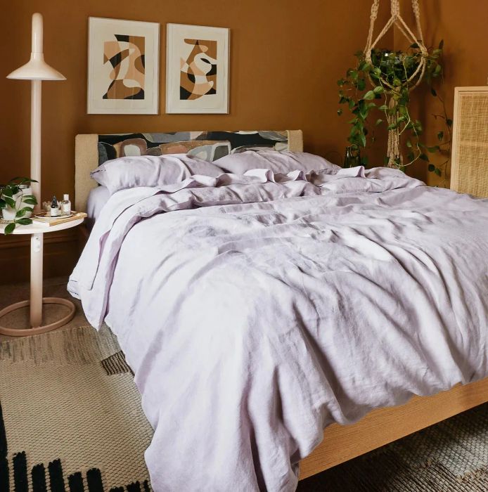 Lilac duvet cover with coordinating sheets and pillowcases on a light wooden bed frame, accompanied by a metal floor lamp beside it.