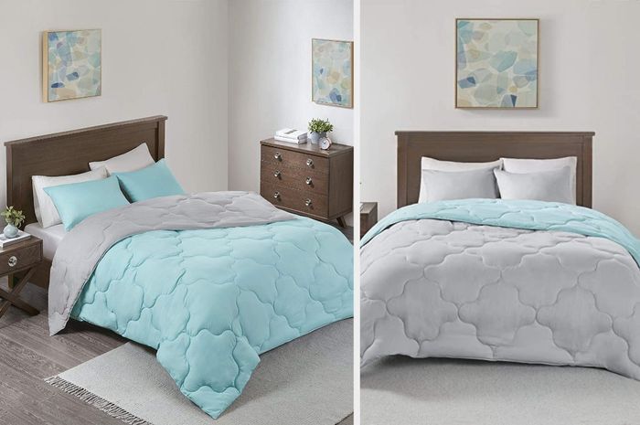A teal tufted comforter with gray sheets and teal and gray pillowcases, placed next to a brown wooden nightstand. The comforter is flipped over to reveal its gray side, with gray pillows resting on top of a gray carpet.